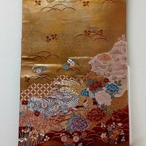 May include: A decorative Japanese scroll featuring a gold background with a detailed floral and landscape design. The artwork includes peonies, birds, and stylized water elements in shades of red, blue, and gold. The scroll is mounted on wooden dowels.