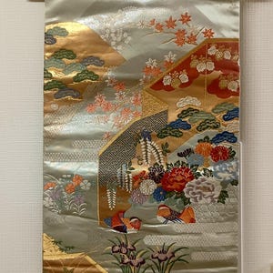 May include: A decorative Japanese wall hanging with a light green background and gold accents. The artwork features colorful floral and bird motifs, with detailed embroidery and a wooden hanging rod.