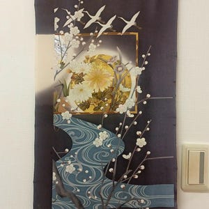 May include: A decorative wall hanging with an Asian-inspired design. The artwork features white cranes, cherry blossoms, and a stylized river against a dark background. The central image includes a golden sun and floral elements.