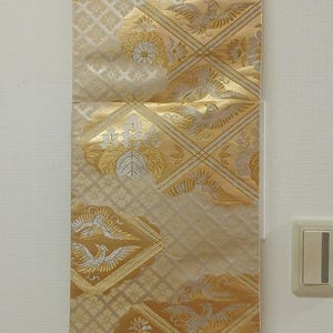 May include: A decorative wall hanging with a gold and cream color scheme. The fabric features a repeating pattern of birds and floral designs. The hanging is suspended from a wooden rod.