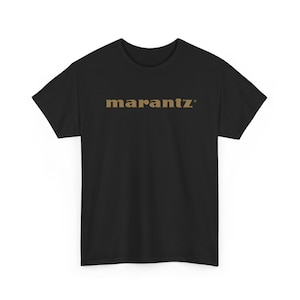 Könnte beinhalten: Schwarzes T-Shirt mit dem Wort "marantz" in goldener Schrift auf der Brust. Das T-Shirt hat kurze Ärmel und einen Rundhalsausschnitt.