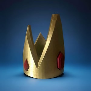 May include: A gold-colored crown with a geometric design. The crown features two red, gem-like accents. The crown is set against a blue background.