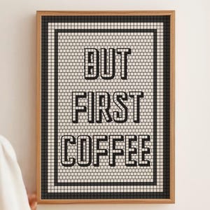 Könnte beinhalten: Gerahmtes Wandbild mit dem Text "BUT FIRST COFFEE" in fetter schwarzer Schrift. Das Kunstwerk hat einen mosaikartigen Hintergrund in Schwarz und Weiß und ist in einem Holzrahmen eingefasst.