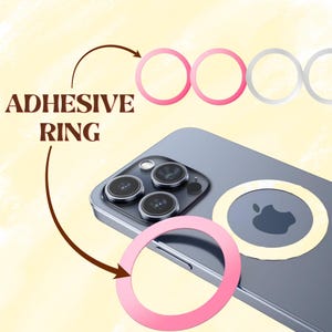 Peut inclure: Illustration d'un smartphone avec un protecteur d'objectif. L'image montre un smartphone argent&eacute; avec une bosse de cam&eacute;ra et un anneau adh&eacute;sif rose. Le texte "ADHESIVE RING" est &eacute;galement visible.