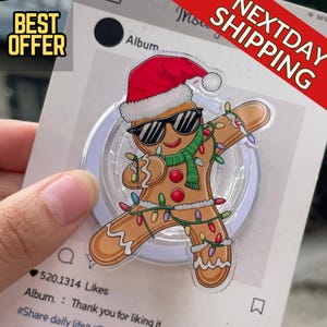 May include: A clear phone grip featuring a gingerbread man wearing sunglasses, a Santa hat, and a green scarf, decorated with Christmas lights. The image includes the text "BEST OFFER" and "NEXTDAY SHIPPING".