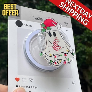 May include: A clear phone grip with a festive ghost design. The ghost wears a Santa hat and is decorated with fairy lights and a candy cane. The grip is on a white Instagram-style card with the text "Best Offer" and "Next Day Shipping".