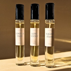 May include: Three perfume bottles with black lids and labels. The labels read "VANILLA TALE", "ROSE STORY", and "NIGHT Blooms". Each bottle contains a light yellow liquid and is labeled "10 ml".