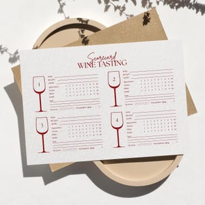 May include: A white rectangular wine tasting scorecard printed with dark red text and graphics. The card features four numbered wine glass illustrations, lines for wine details, numerical rating scales from 1 to 10, and heart icons for scoring.