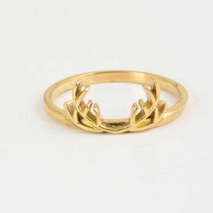 May include: A gold-colored ring featuring a detailed antler design. The ring is made of a shiny, metallic material and is set against a plain white background. The antlers are the focal point, adding a touch of nature-inspired elegance.