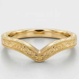 May include: A gold-colored, V-shaped ring with intricate floral and scrollwork engravings. The ring's design features a curved band that tapers to a point, creating a unique and elegant look. The ring is likely made of gold and is designed to be worn as a wedding band.