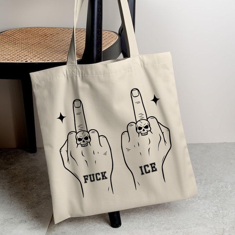 May include: Beige tote bag featuring a black graphic of two hands with middle fingers extended, each wearing a skull ring. The word "FUCK" is below one hand, and "ICE" is below the other. Black starbursts are on either side.