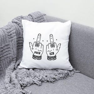 May include: White square pillow with a black graphic of two hands giving the middle finger. The word "FUCK" is printed below one hand, and "ICE" below the other. The hands wear rings and bracelets.
