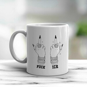 May include: White ceramic mug featuring a black and white illustration of two hands giving the middle finger. The hands are adorned with rings, bracelets, and long black fingernails. The words "FUCK ICE" are printed below the hands.