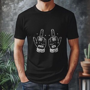May include: Black t-shirt with a white graphic of two hands displaying the middle finger. The text "FUCK ICE" is printed below the hands. The hands are adorned with rings and bracelets.