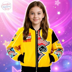 May include: A yellow bomber jacket with black accents and colorful graphic designs. The jacket features the word "rrumi" on the front and a zipper closure. The sleeves have additional graphic details. The jacket is worn by a person.