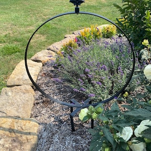 Könnte beinhalten: Schwarze Metall-Gartenpflanzenstütze mit kreisförmigem Rahmen und Lilien-Spitze. Die Stütze befindet sich in einem Blumenbeet mit Lavendel und anderen bunten Blumen. Die Stütze ist etwa 122 cm hoch.