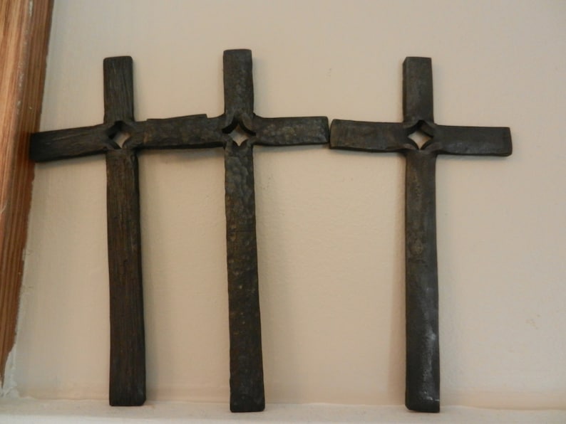 Peut inclure: Trois croix en m&eacute;tal gris fonc&eacute; avec une d&eacute;coupe en forme de losange &agrave; l'intersection des bras. Les croix sont mont&eacute;es sur un mur beige clair. Les croix ont un aspect rustique et textur&eacute;.