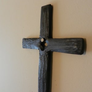 Peut inclure: Une croix en bois gris fonc&eacute; avec une surface textur&eacute;e est fix&eacute;e sur un mur beige clair. La croix a un design simple et rustique avec une poutre verticale et une poutre horizontale. La croix est un symbole de foi et de spiritualit&eacute;.