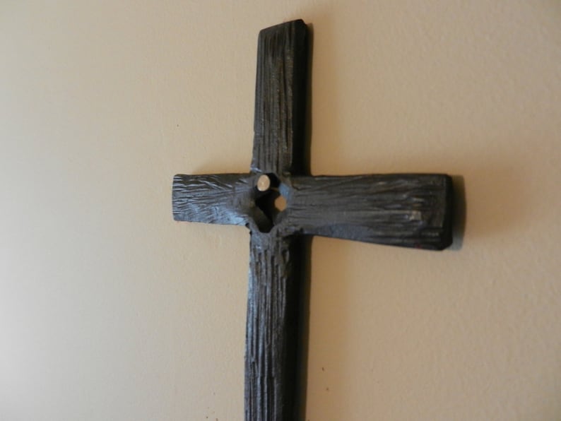 Peut inclure: Une croix en bois gris fonc&eacute; avec une surface textur&eacute;e est fix&eacute;e sur un mur beige clair. La croix a un design simple et rustique avec une poutre verticale et une poutre horizontale. La croix est un symbole de foi et de spiritualit&eacute;.