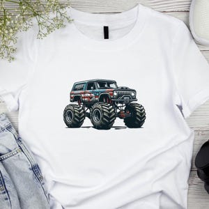Puede incluir: Camiseta blanca con un gr&aacute;fico de un monster truck. El cami&oacute;n tiene un dise&ntilde;o azul, rojo y blanco con un tema de bandera estadounidense. La camiseta est&aacute; hecha de un material suave. El cami&oacute;n tiene neum&aacute;ticos grandes.