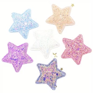 Könnte beinhalten: Ein Set aus sechs sternförmigen Haarspangen mit glitzernder Oberfläche in verschiedenen Farben wie Hellblau, Pfirsich, Weiß, Lila und Pink. Jeder Stern hat eine texturierte, funkelnde Oberfläche und eine kleine Metallspange auf der Rückseite.