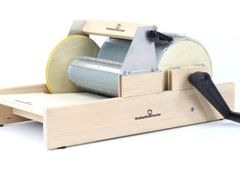 May include: A wooden hand carder with a black handle and a metal carding cylinder. The carder is made by Brother/Sister/Carder.