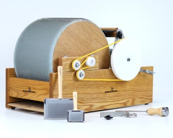 May include: A wooden wool carding machine with a gray carding cylinder, a white drive wheel, and a yellow belt. The machine is on a wooden base with the text "Brother's Craft Center" printed on it. The machine is accompanied by a set of tools including a wooden brush, a metal comb, and a metal hook.