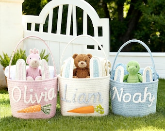 May include: Three Easter baskets in pink, white, and blue, each with a stuffed animal and bunny ears. The pink basket says "Olivia", the white basket says "Liam", and the blue basket says "Noah". Each basket has a carrot applique.