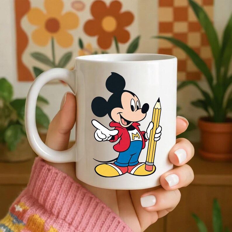 Op de afbeelding: Witte keramische mok met een kleurrijke illustratie van Mickey Mouse die een gele potlood vasthoudt. Mickey draagt een rode jas, een blauwe broek en gele schoenen. De mok heeft een gebogen handvat.