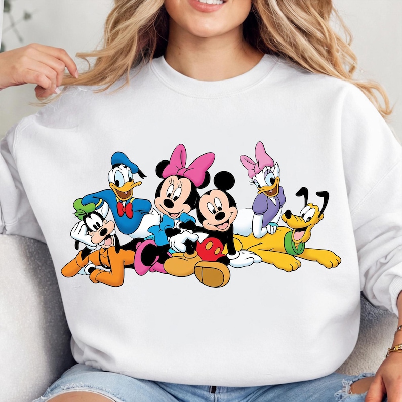 May include: White sweatshirt featuring a colorful graphic of Disney characters, including Mickey and Minnie Mouse, Donald Duck, Goofy, Daisy Duck, and Pluto. The cartoon characters are in a group, with vibrant colors and distinct features.