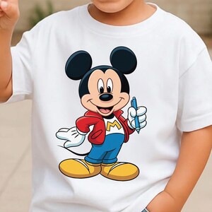 Op de afbeelding: Wit T-shirt met een Mickey Mouse-afbeelding. Mickey draagt een rode jas, een blauwe broek en gele schoenen, en houdt een blauwe pen vast. Het ontwerp bevat de letter "M" op de jas. Een klassiek cartoon-personage-ontwerp.