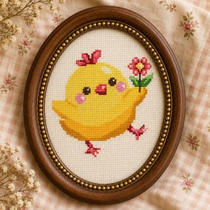 May include: Oval framed cross-stitch art featuring a yellow chick holding a pink flower. The chick has pink cheeks and a red bow. The frame is brown with a gold beaded inner border. The background is a cream-colored fabric.