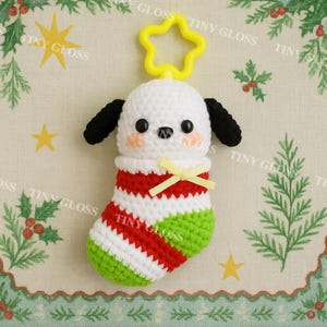 May include: A crocheted Christmas stocking featuring a white dog with black ears and a yellow star-shaped keychain. The stocking is striped red, white, and green, with a yellow bow. The dog has pink cheeks and black eyes.