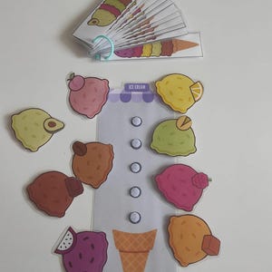 May include: An ice cream-themed educational toy set. Includes a cone, various ice cream scoop designs, and a booklet of ice cream cone illustrations. The set features colorful illustrations of different ice cream flavors and toppings.