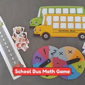 Puede incluir: Un juego de matemáticas con un recorte de autobús escolar amarillo, un recorte de autobús verde, un tablero de juego rectangular con forma de carretera y una escuela, fichas cuadradas y dos ruletas circulares con números y símbolos.