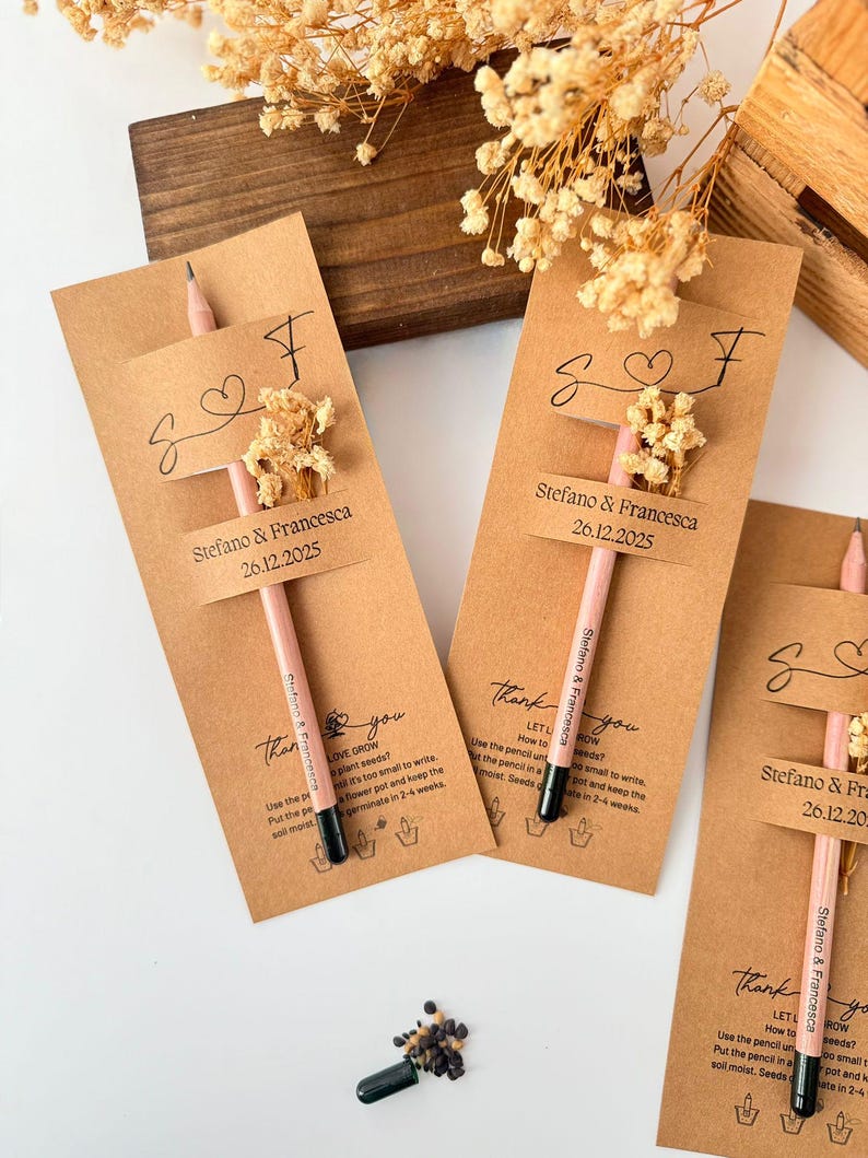 May include: Kraft paper wedding favors with pink pencils, dried flowers, and personalized tags. Each tag reads "Stefano & Francesca 26.12.2025" and includes instructions for planting seeds. A charming and unique wedding favor.