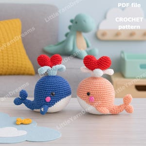 May include: Two crocheted whale toys, one blue and one peach, each with a red heart-shaped spout. The whales have white bellies and pink cheeks. The image also includes a small yellow fish and text that says "PDF file CROCHET pattern."