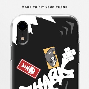 May include: Clear phone case with a black background and a shark-themed design. The case features a cartoon shark, fish bones, and the word "SHARK" in white graffiti-style lettering. The text "MADE TO FIT YOUR PHONE" is at the top.