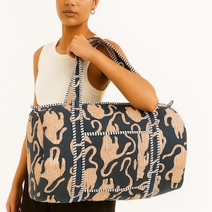 Könnte beinhalten: Eine marineblaue und beige Reisetasche mit einem sich wiederholenden Tiermuster. Die zylindrische Tasche hat eine Reißverschlusstasche und gestreifte Akzente. Die Griffe sind ebenfalls gestreift.