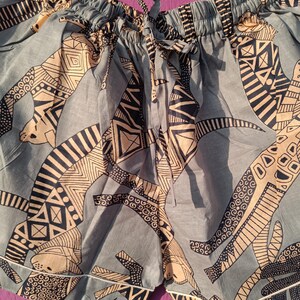 May include: Blue patterned shorts with a drawstring waist and white trim. The shorts feature a repeating design in tan and black. The fabric appears to be lightweight, suitable for warm weather. The shorts are hanging on a metal hanger.