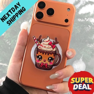 Könnte beinhalten: Orangefarbene Handyhülle mit einem Cartoon-Motiv einer heißen Schokoladentasse mit Rentiergeweih und einem Zuckerstangen-Strohhalm. Die Hülle hat einen integrierten Handyhalter. Die Worte "NEXTDAY SHIPPING" stehen in einem blauen Banner.