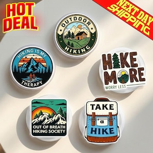 May include: A collection of hiking-themed circular and square stickers. Designs include mountain landscapes, text like "Hiking is my therapy," and a backpack graphic. Colors include blue, orange, green, and brown.