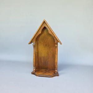 以下が含まれることがあります： 尖ったゴシックアーチ型の頂部、平らな基部、屋根構造を支える2本の細い旋盤加工された柱を備えた木製の壁掛け棚。木材はミディアムブラウンの仕上げで、構造全体に木目がはっきりと見えています。