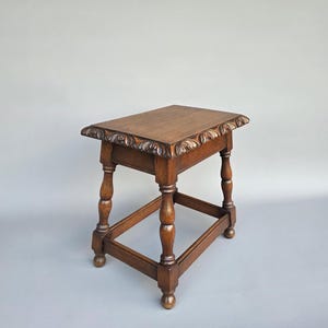 Op de afbeelding: Een kleine, antieke houten bijzettafel met een rechthoekig blad en gesneden bloemmotieven. De tafel heeft vier gedraaide poten en een onderste spijl voor extra stabiliteit. Het hout heeft een warme, bruine tint. Afmetingen: ongeveer 40 cm x 30 cm x 50 cm.