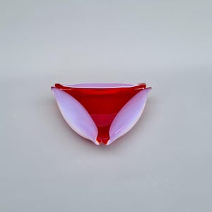 Könnte beinhalten: Eine dekorative Glasschale mit einem Blütenblatt-Design. Die Schale hat einen leuchtend roten Innenraum und zart lavendelfarbene Blütenblätter. Die Form der Schale erinnert an eine Blume und verleiht jedem Raum Eleganz.