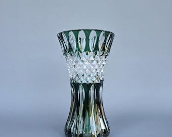 May include: A decorative green and clear glass vase. The vase has a flared top and a diamond-cut pattern in the middle. The base is a darker green, and the top rim is also green. The vase is approximately 10 inches tall.