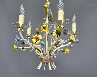 May include: A vintage white metal chandelier with five candle-style lights. The chandelier is adorned with colorful, hand-painted flowers in yellow, blue, and green. The light fixtures have a cream-colored finish and are suspended from a chain.