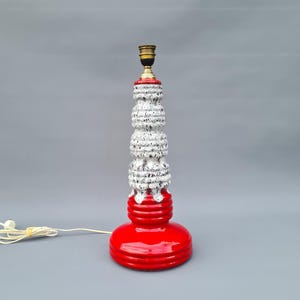 Op de afbeelding: Een hoge keramische tafellamp met een rode voet en een getextureerde, wit en zwart gespikkelde behuizing. De lamp heeft een messingkleurige fitting en een wit snoer. De hoogte van de lamp is ongeveer 46 cm.