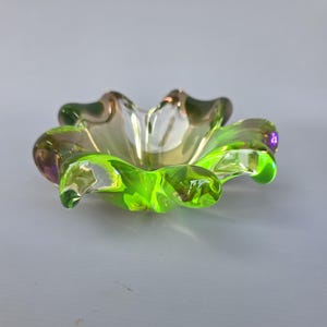 Puede incluir: Un pequeño cuenco de cristal festoneado con un borde verde lima vibrante que se transforma en un centro ámbar pálido translúcido. El cuenco tiene un borde orgánico ondulado con seis curvas distintas en forma de pétalo.