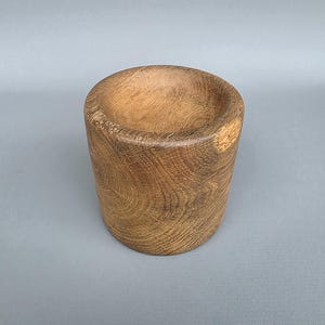 Op de afbeelding: Een cilindrische houten kom met een afgeronde binnenkant. De kom is gemaakt van lichtbruin hout met zichtbare nerfpatronen. De kom wordt waarschijnlijk gebruikt om te serveren of tentoon te stellen.